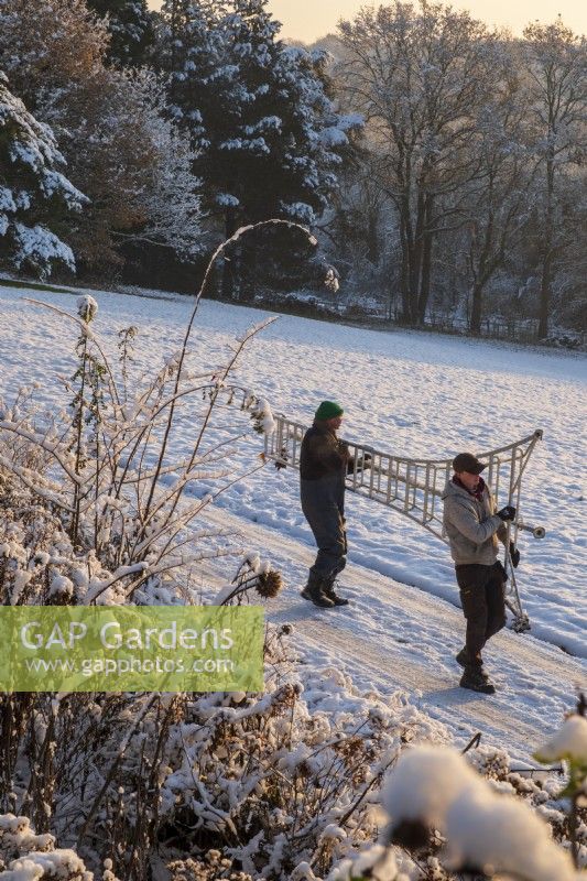 The garden at Gravetye Manor, Sussex, in winter, gardeners carrying ladders through a snowy garden