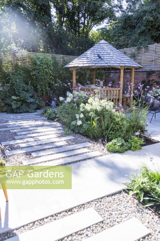 Garden with stone tile patio, staggered tile path, a round wooden gazebo and a bed in the middle with mixed planting