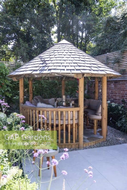 Round wooden gazebo with tile roof and seating inside
