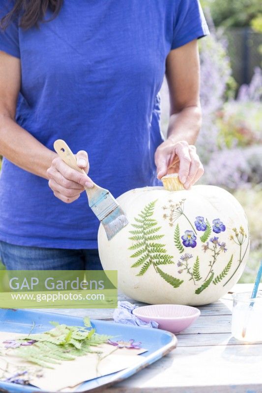 Woman using a wide brush to spread glue over the whole pumpkin as a glaze