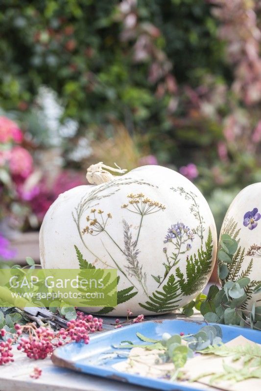 White pumpkins with pressed flowers and leaves on table with berries and eucalyptus sprigs