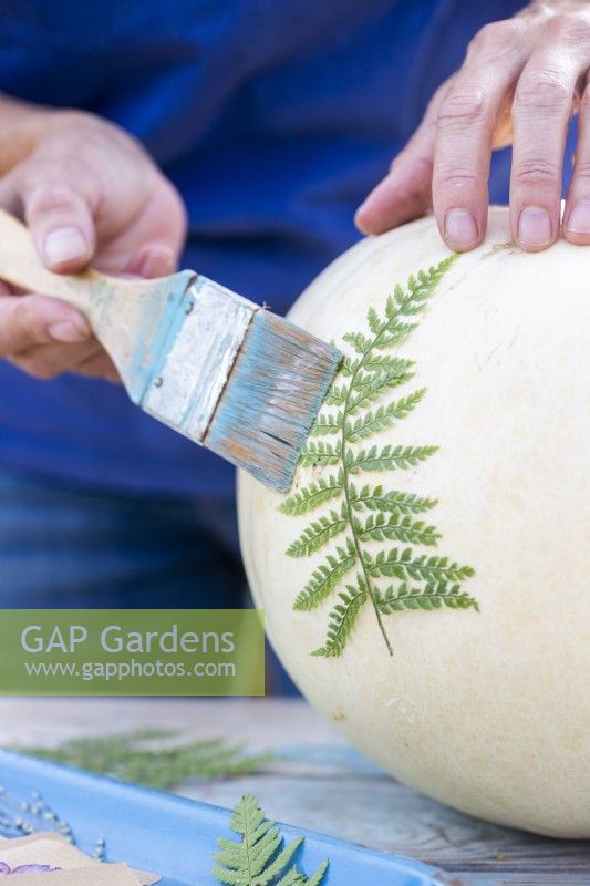Woman brushing glue over fern to stick it to the pumpkin
