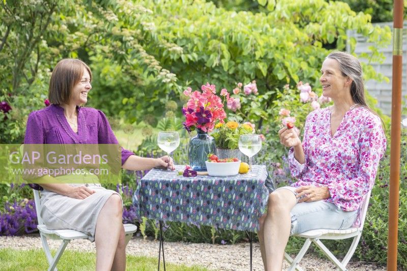 Women sitting at table with drinks, strawberries and a bouquet of Sweet peas and Clematis