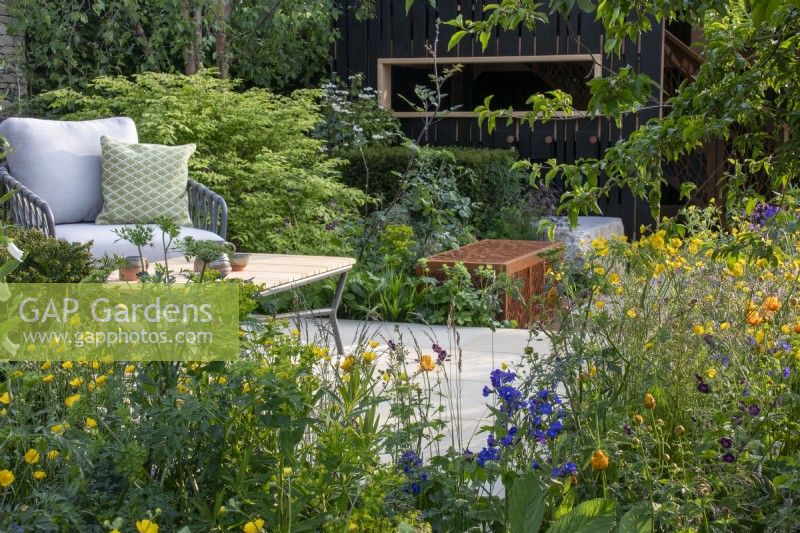 A seating area and table surrounded by naturalistic planting on the RSPCA Garden designed by Martyn Wilson - RHS Chelsea Flower Show 2023