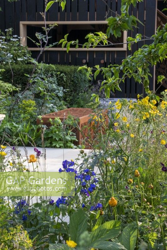 View across borders and paving towards a Corten steen dead hedge box and wooden wildlife hide on the RSPCA Garden designed by Martyn Wilson - RHS Chelsea Flower Show 2023