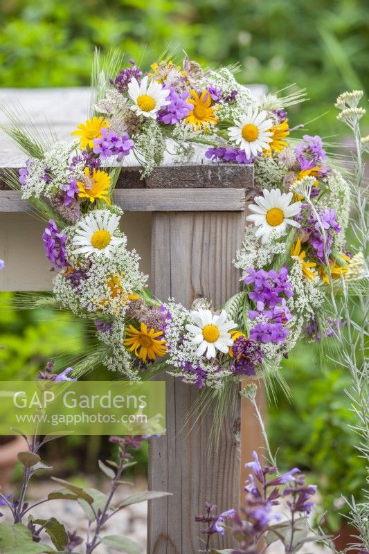 Wildflower wreath made of daisies,  wild onions, cow parsley, wheat  and  yellow ox-eye hanging from the table.