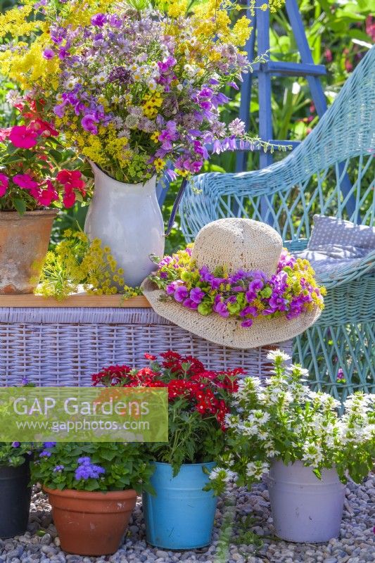 Display of pots with balcony flowers, hat with wreath and flower bouquet of sweet peas and wildflowers in enamel jug.