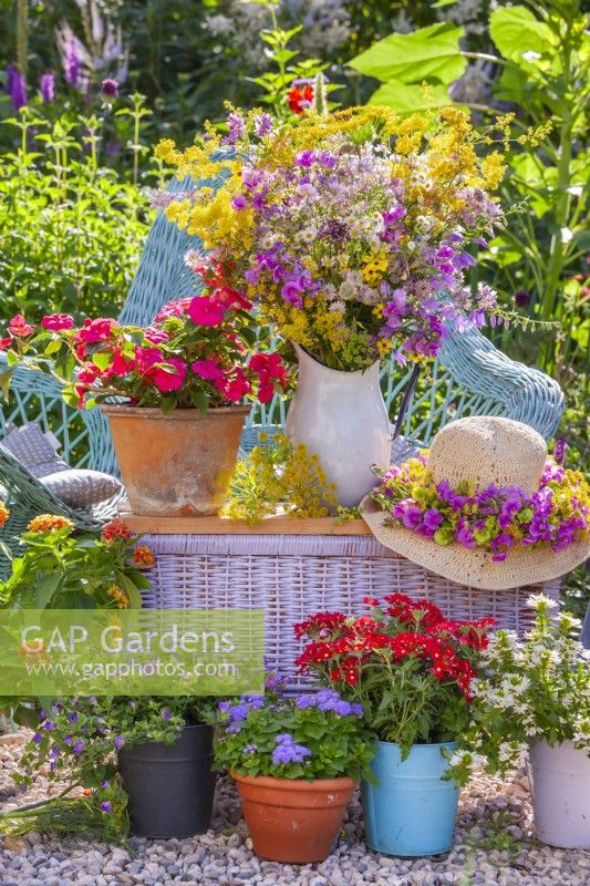 Display of pots with balcony flowers, hat with wreath and flower bouquet of sweet peas and wildflowers in enamel jug.