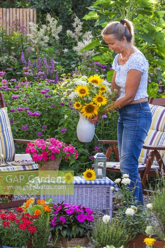 Woman making a floral arrangement with sunflowers on terrace with many containers planted with herbs and balcony flowers.