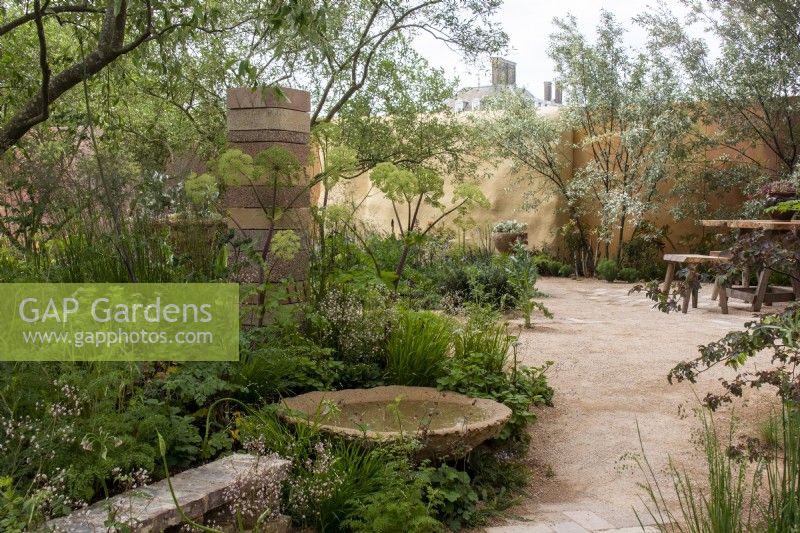 View through The Nurture Landscapes Garden  with a circular water feature, wall and column made from waste materials- designer Sarah Price - RHS Chelsea Flower Show 2023