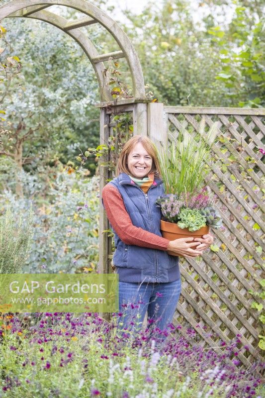 Woman carrying a terracotta pot planted with Ornamental Kale, Ornamental grasses and callunas