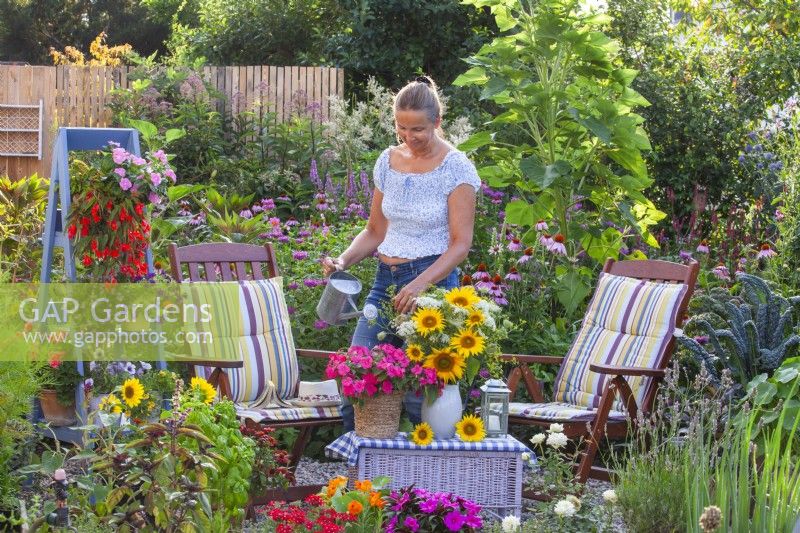 Woman watering Impatiens in pot next to bouquet with sunflowers and  wild carrots.