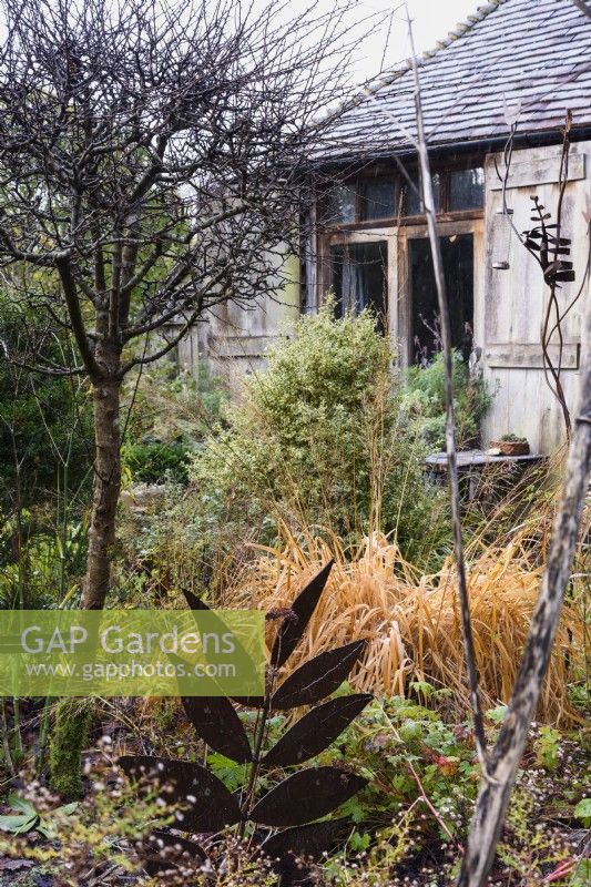 Decorative metal leaf amongst shrubs and grasses in the garden of Balmoral Cottage in December