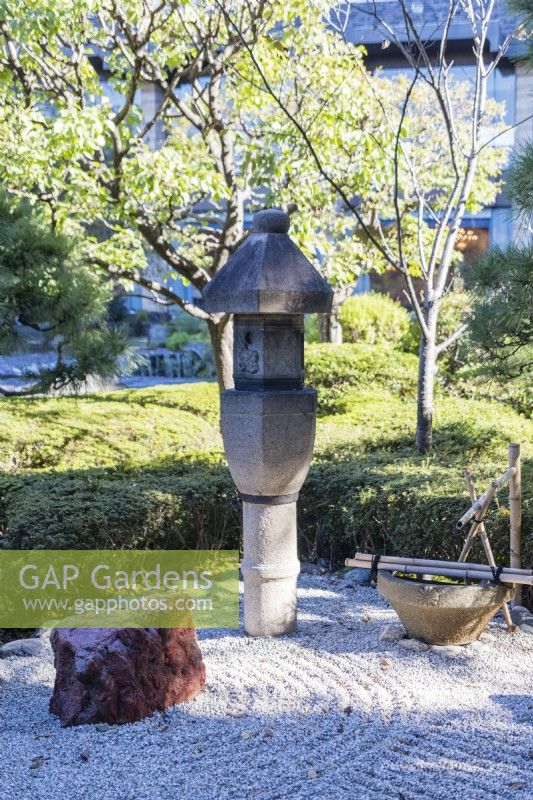 Stone lantern, or ishidoro, in raked gravel with placed rock with bamboo water fetaure. 