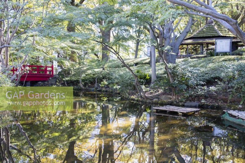Red painted wooden bridge over the Seisen pond, reflected in the water and view to the garden chapel.