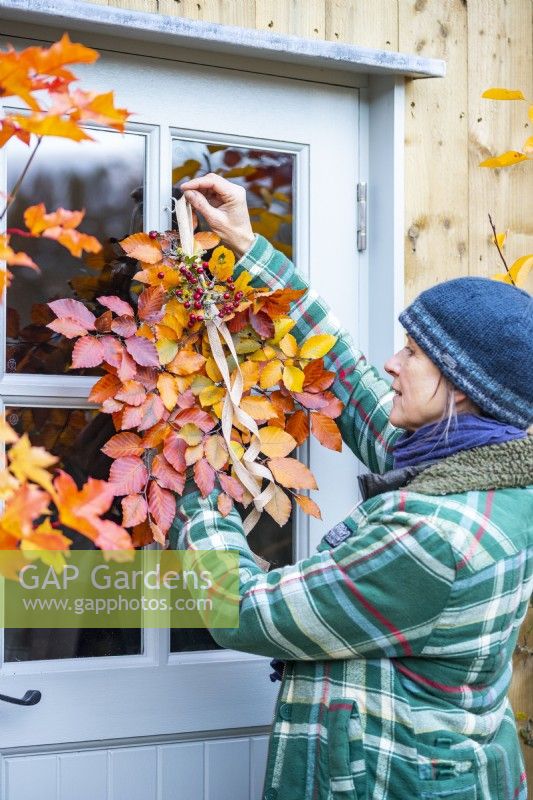 Woman hanging up arranged Beech sprigs and Hawthorn berries on door