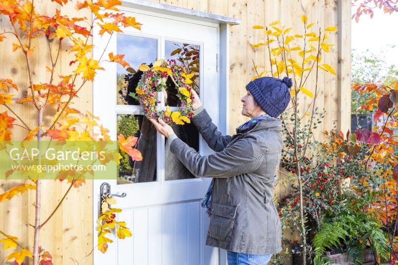 Woman placing wreath made out of Ivy, Beech sprigs and Hawthorn on a door