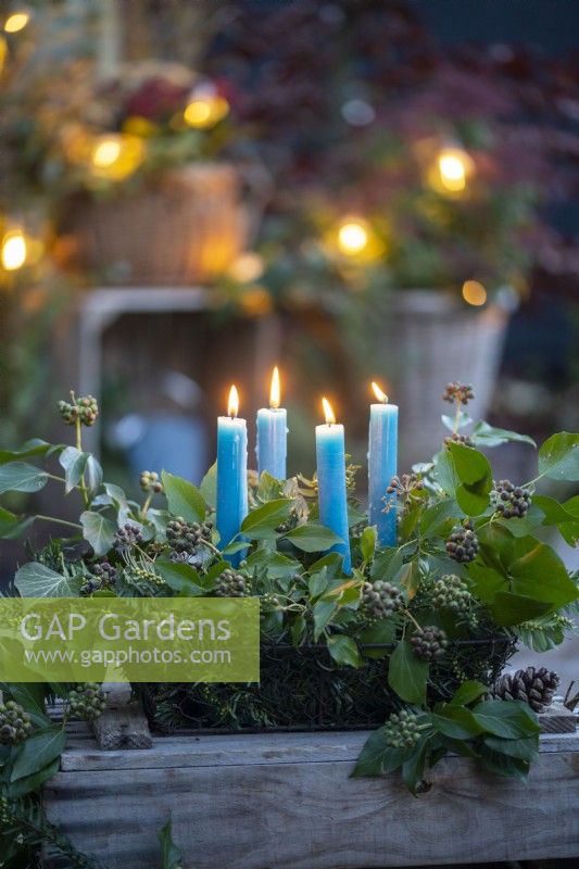 Candles in metal basket with Ivy Hedera, Yew sprigs and pinecones on wooden crate