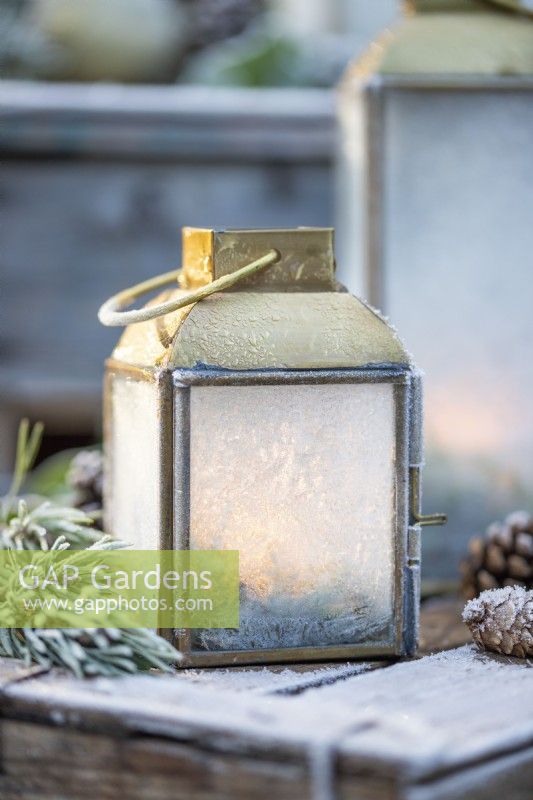 Small lantern frosted over with Pine sprigs and pinecones on wooden crates