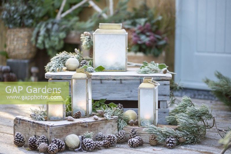Small lanterns frosted over with Pine sprigs, pinecones and Baubles on wooden crates