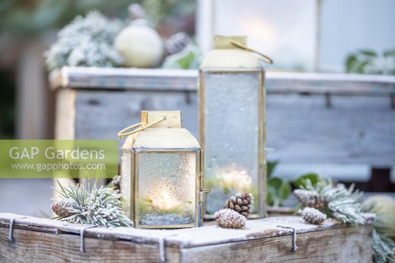 Small lanterns frosted over with Pine sprigs and pinecones on wooden crates