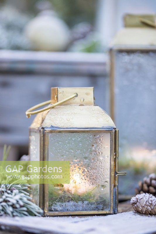 Small lanterns with water on glass from melted frost with Pine sprigs and pinecones on wooden crates - covered in frost