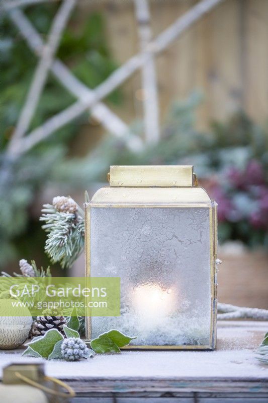 Lantern frosted over with Pine sprigs, pinecones and baubles on wooden crates