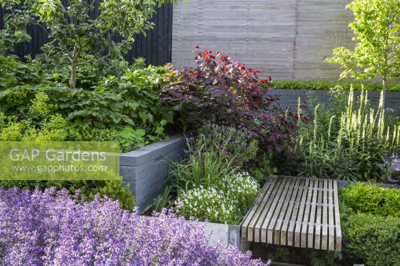 Slatted floating bench amid lushly planted summer raised beds