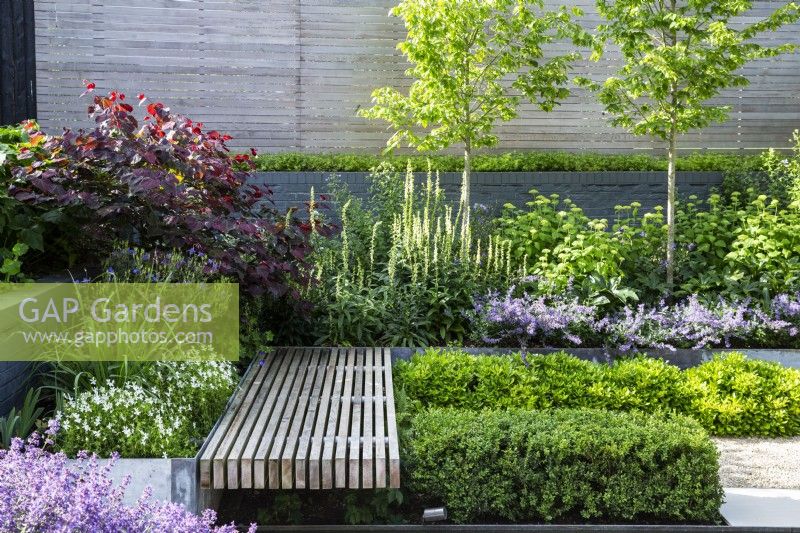 Lushly planted raised beds around floating wooden bench in modern garden