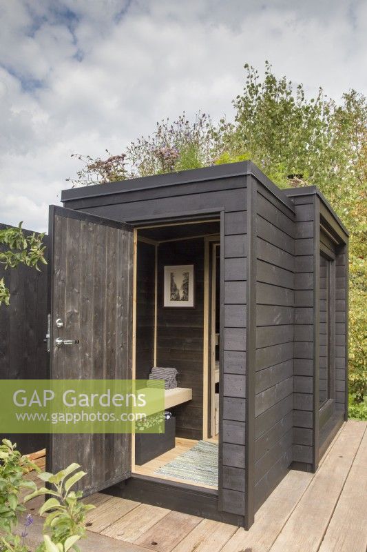 Timber wooden deck with black painted wood sauna cabin with a living roof planted with wildflowers and herbs  - The Finnish Soul Garden RHS Chelsea Flower Show September 2021 