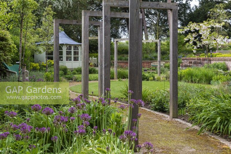 Oak frames straddle a path that meanders through a contemporary garden with circular lawns, and borders planted with alliums, geums and leafy perennials to flower later.