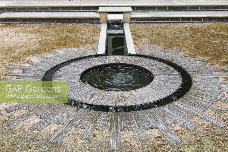 A rill with metal casings that lead into double circles. The circular water feature is set into a sun style design created from laying slates on their sides.