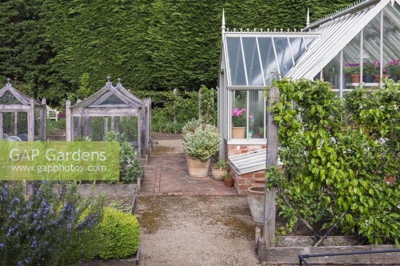 A formal kitchen garden with cold frame and espaliered fruit trees outside a greenhouse. Four square bespoke oak cloches protect vulnerable crops.