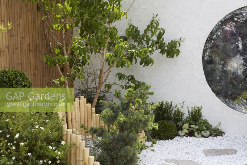 The Lunar Garden Designer: Queenie Chan. Low bamboo fence with white gravel and white wall containing round antique mirror glass.