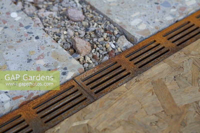 Detail of drainage areas in patio/pathway. Rusty metal grille and gravel drainage. 