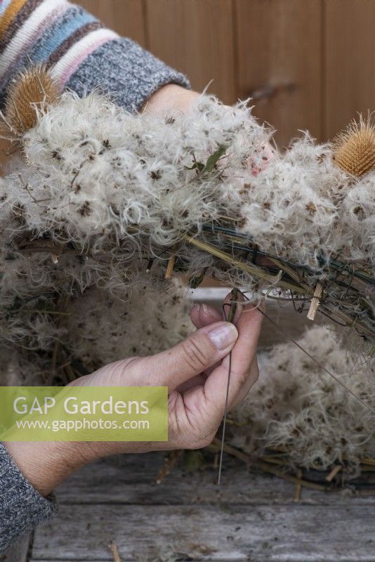 Step-by-Step making a Countryside Wreath from a wire frame wrapped in old man's beard. Step 4: attach wired berries and seedheads to the underside of the frame.