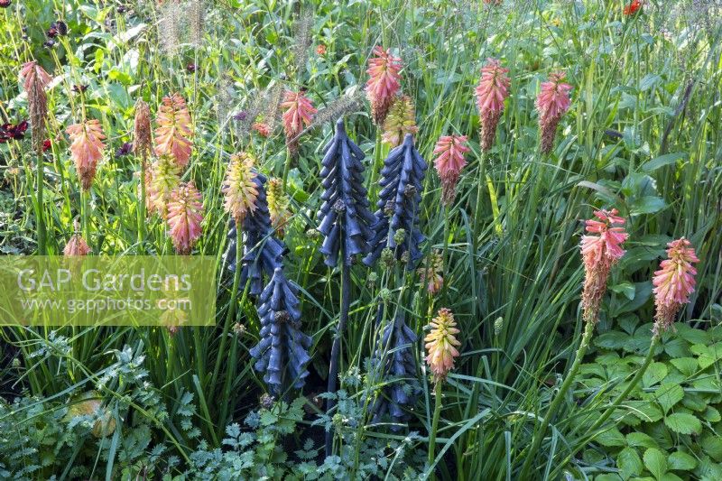Black metal sculpture of Kniphofia - red hot pokers with planting of Kniphofia and Pennisetum alopecuroides 