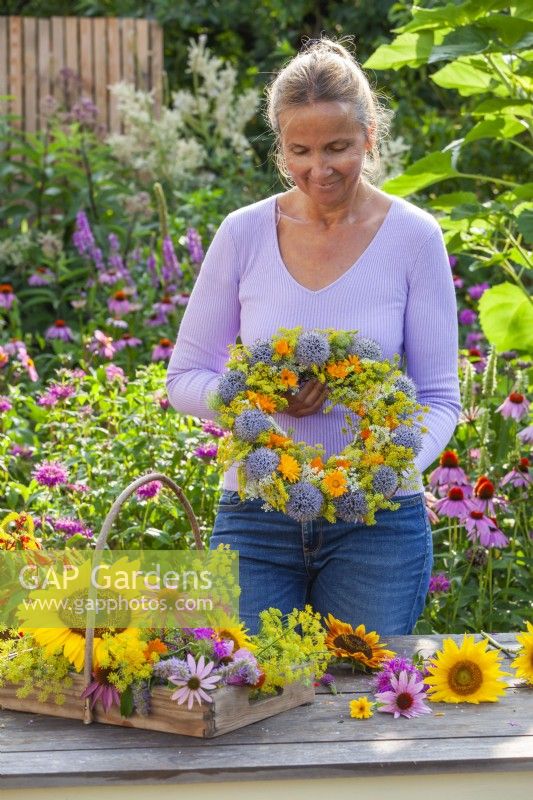 Woman making wreath using pot marigold, fennel, coneflower, globe thistles and wild carrots.