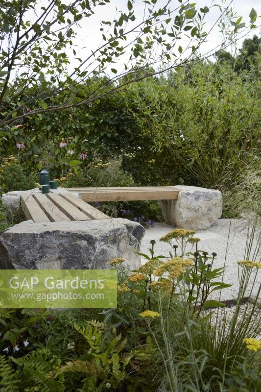 Inghams Working with Nature Garden. Designers: Joshua Parker and Matthew Butler. Seating area. Beams of wood inlaid on rock to form seats surrounded by naturalistic planting. Summer.
