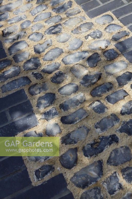 Mottled shadows over pathway of inlaid flint edged with black bricks.