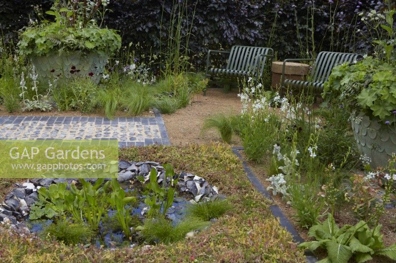 The Traditional Townhouse Garden. Designer: Lucy Taylor. Seating area by round pond edged with knapped flint bordered by a carpet of sedum. Aquatic plants include Pontederia cordata - pickerel weed - and Pistia stratiotes - water lettuce. Summer.