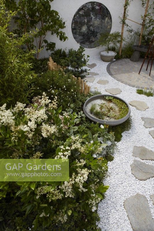The Lunar Garden Designer: Queenie Chan. Low bamboo fence by white themed border with white gravel and white wall containing round antique mirror glass.