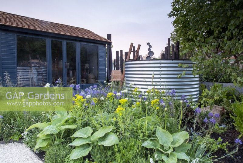 Summerhouse with a border mixed perennial planting of Hosta 'T-Rex', Allium nigrum, Euphorbia and Camassia 