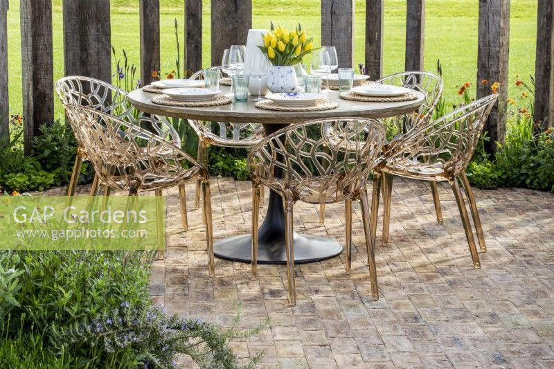 Modern plastic chairs and laid out round dining table on a brick paved patio