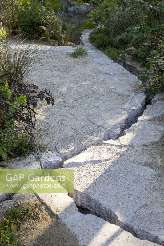Modern contemporary path made from salvaged reclaimed concrete with a water rill in the cracks running through the garden
