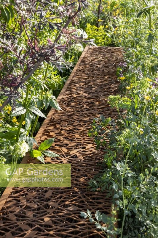 Laser cut corten steel dead hedge for filling with garden prunings that create habitats for beneficial insects surrounded by mixed perennial planting and wildflowers 