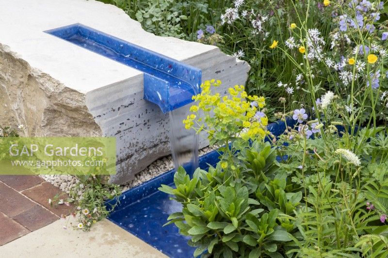 A modern contemporary water rill made from recycled plastics set in stone - mixed perennial planting Euphorbia robbiae, Geranium pratense 'Mrs Kendall Clark' and Lychnis flos-cuculi 