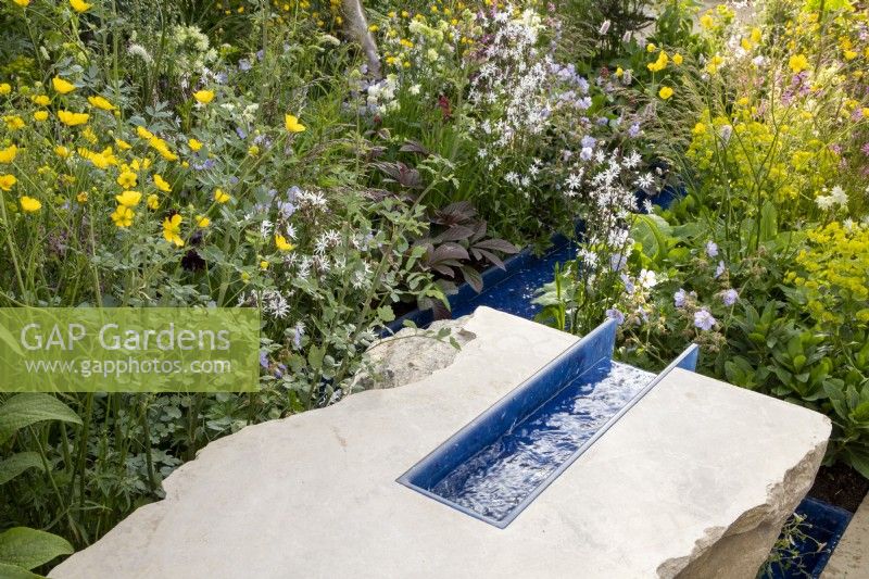 A modern contemporary water rill made from recycled plastics set in stone, mixed perennial planting of Euphorbia robbiae, Geranium, Lychnis flos-cuculi 'White Robin' and Ranunculus acris 