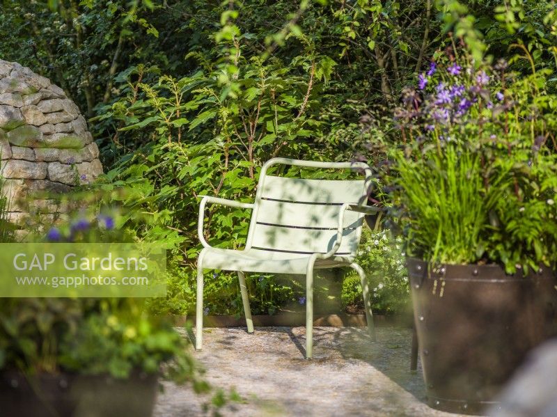 Seating area with Green Fernob chair next to metal container with flowering plants at Horatio's Garden, Chelsea Flower Show 2023. Designer: Charlotte Harris and Hugo Bugg, Gold medal winner, Best Show Garden