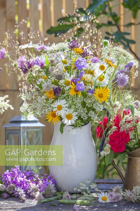 Summer flower arrangement with wildflowers including daisies, yellow ox-eye, wild carrots, campanula, allium and red roses.